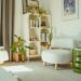 Bright cozy apartment room with white organic bookcase filled with books and plants, fluffy armchair nearby
