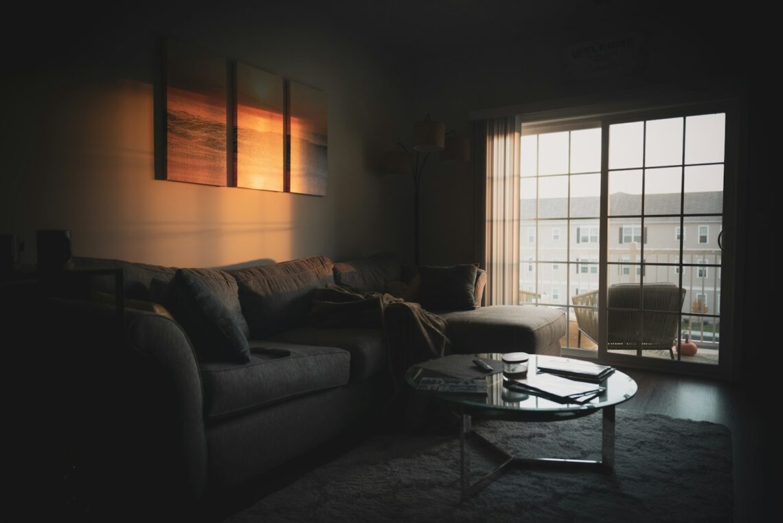 Cozy apartment living room with warm golden light glowing through large window and sectional sofa