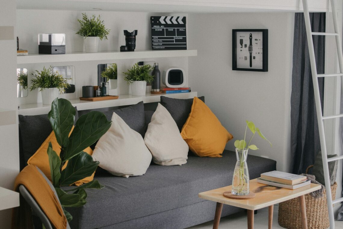 Cozy small studio apartment living room with wall shelves holding plants and gadgets, grey sofa with mustard yellow pillows