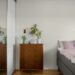 Small apartment bedroom with a wooden dresser topped with potted plants beside a bed with pink bedding