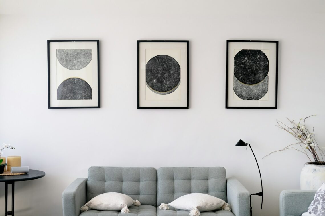 Three framed abstract art pieces hung above a gray sofa in a minimalist apartment living room