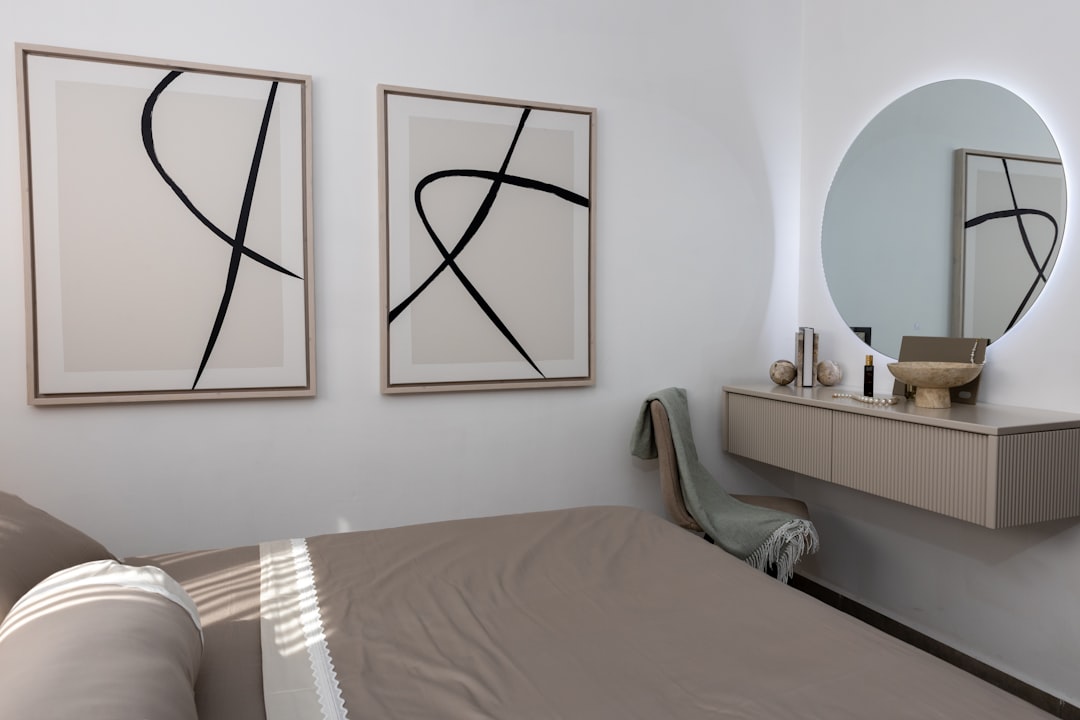 Minimalist bedroom wall with two large abstract line art prints in wooden frames beside a round LED-backlit mirror above a vanity