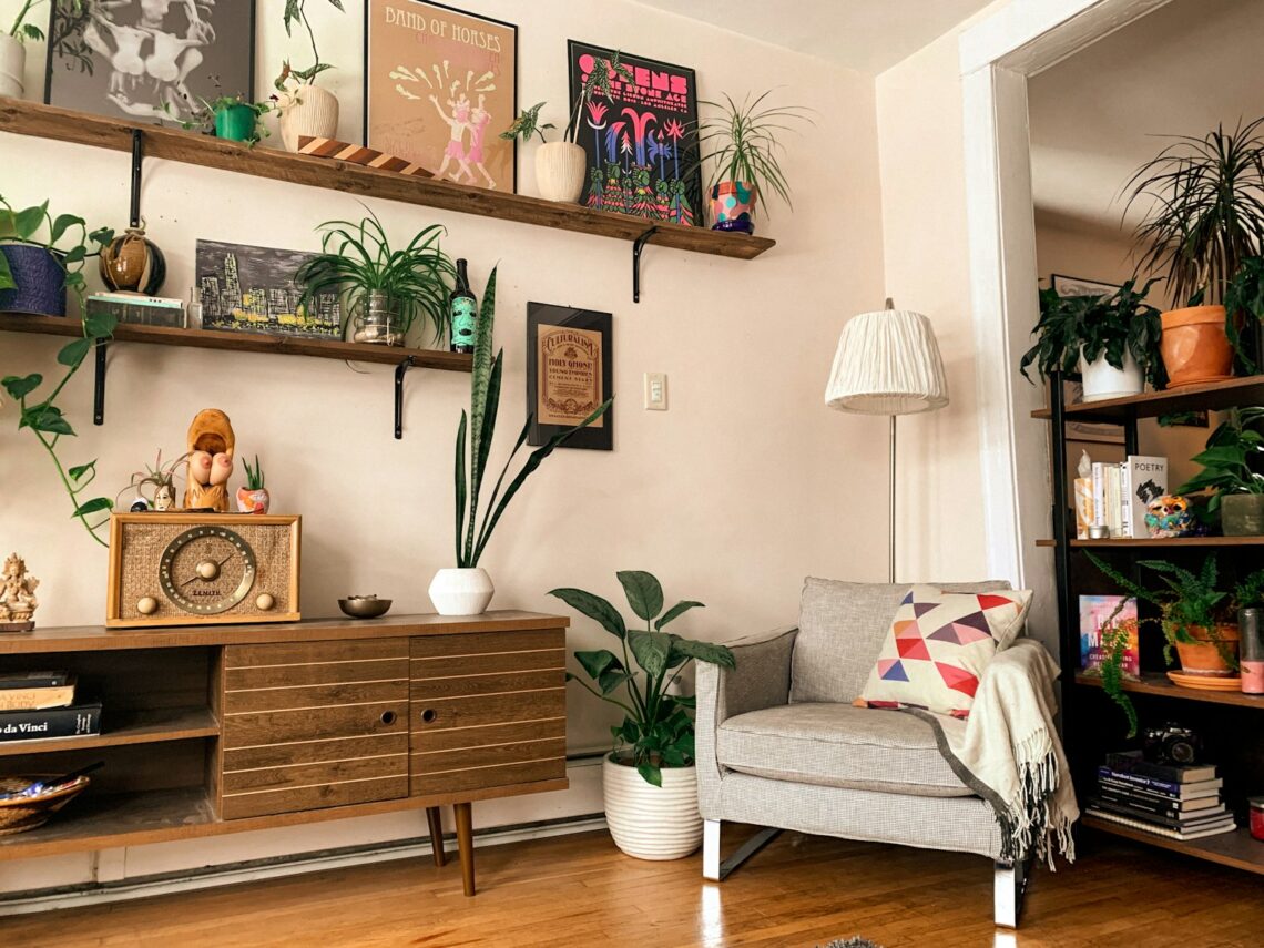 Cozy apartment living room corner with floating wall shelves displaying art prints and potted plants above a wooden sideboard