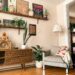 Cozy apartment living room corner with floating wall shelves displaying art prints and potted plants above a wooden sideboard