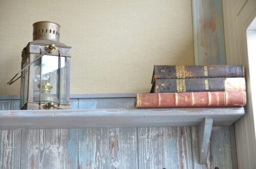 Antique lantern and vintage leather-bound books on a rustic wooden shelf, cottagecore reading nook styling