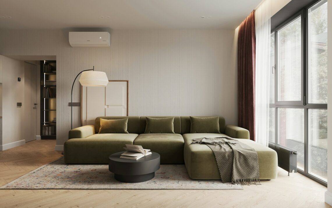 Modern apartment living room with green sectional sofa, throw blanket, and large windows with burgundy curtains