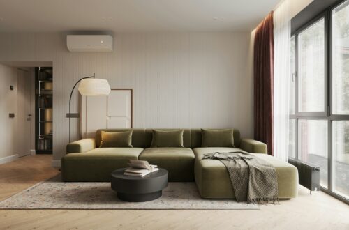 Modern apartment living room with green sectional sofa, throw blanket, and large windows with burgundy curtains