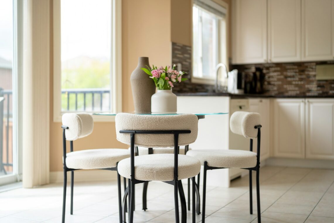 Small round dining table with three white boucle chairs next to a kitchen in a compact apartment