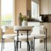 Small round dining table with three white boucle chairs next to a kitchen in a compact apartment