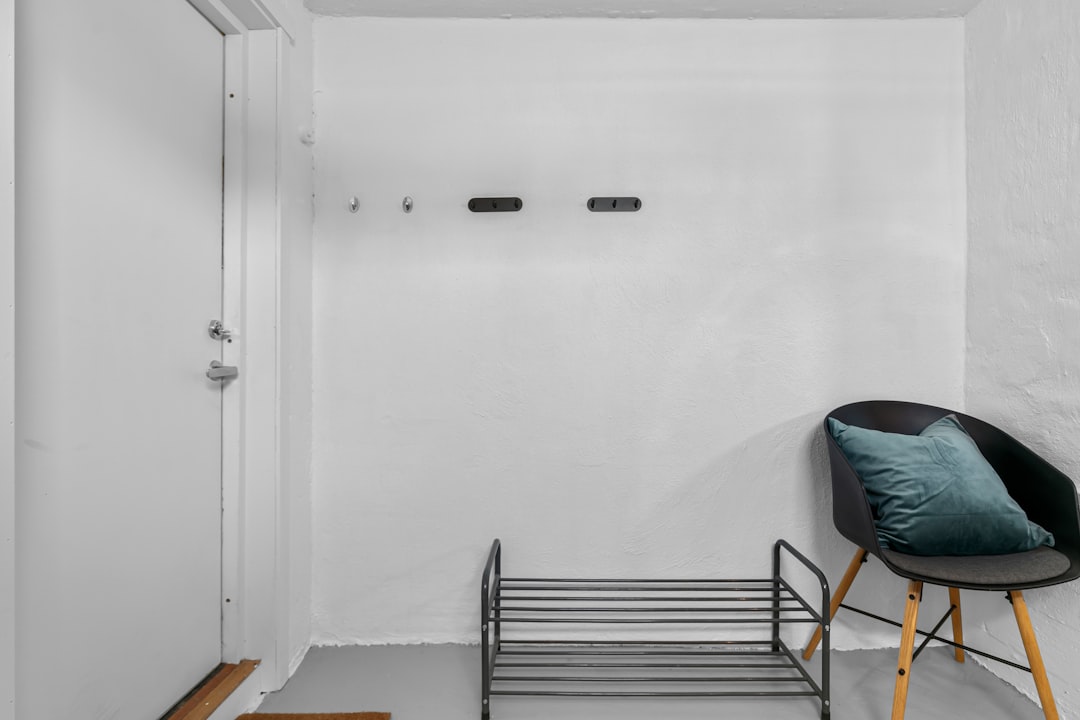 Minimal white apartment entryway with wall hooks, metal shoe rack, and black chair near door