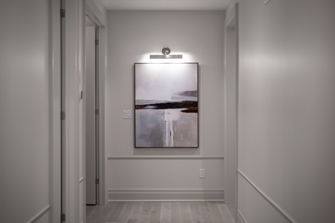 Narrow apartment hallway with abstract landscape painting lit by picture rail light