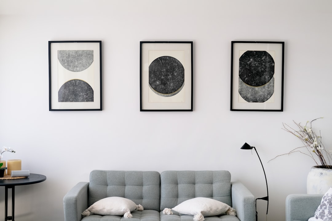 Three matching abstract art prints in black frames hanging in a row above a gray sofa in a modern apartment living room