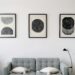 Three minimalist abstract prints above a gray sofa in a modern apartment living room