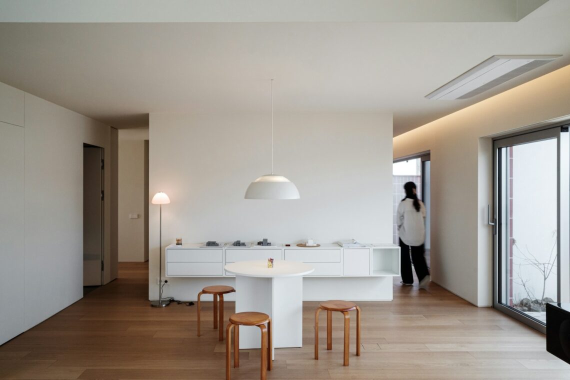 Japandi small apartment dining nook with light oak floor, paper globe pendant, white walls, small round table, and stacked beech wood stools