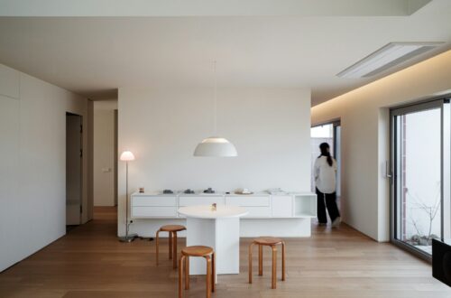 Japandi small apartment dining nook with light oak floor, paper globe pendant, white walls, small round table, and stacked beech wood stools
