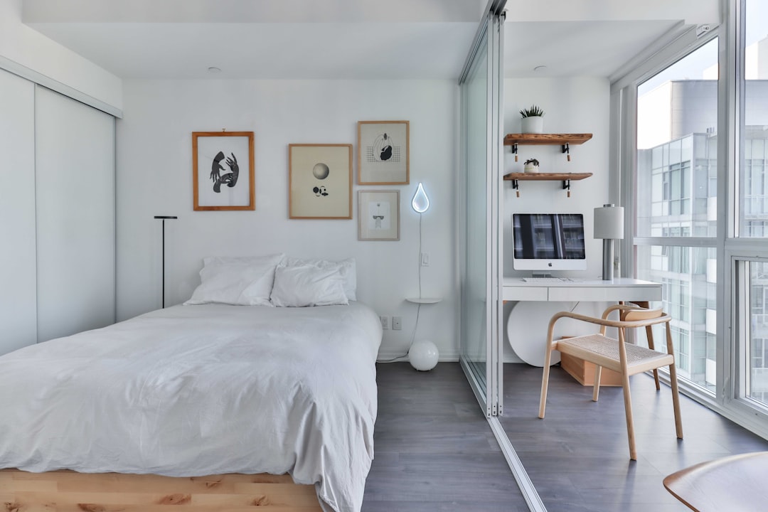 Minimalist apartment bedroom with gallery wall of three framed art prints, floating wood shelves with plants, and a neon teardrop lamp