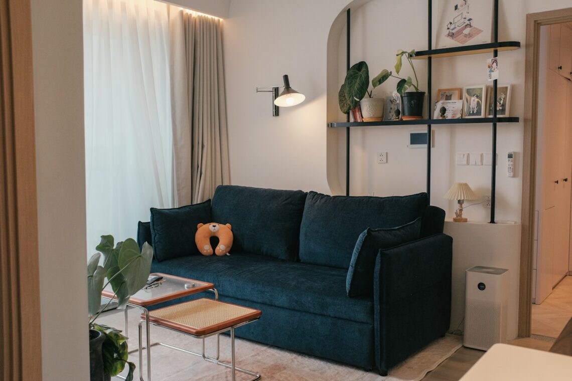 Small apartment living room with navy blue sofa, swing-arm lamp, and cane side table in mid-century modern style