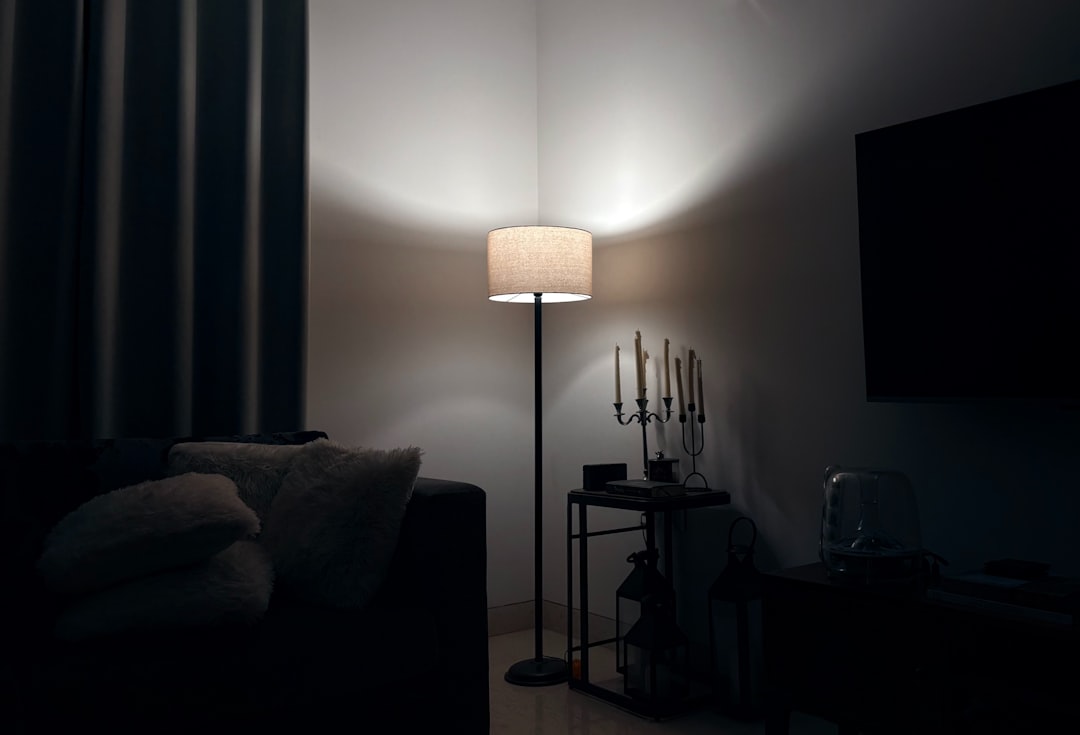 dark apartment living room corner with floor lamp casting warm light on sofa and candle holder