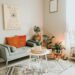 Cozy NYC-style apartment living room with plants, a grey sofa, orange pillows, and boho rug