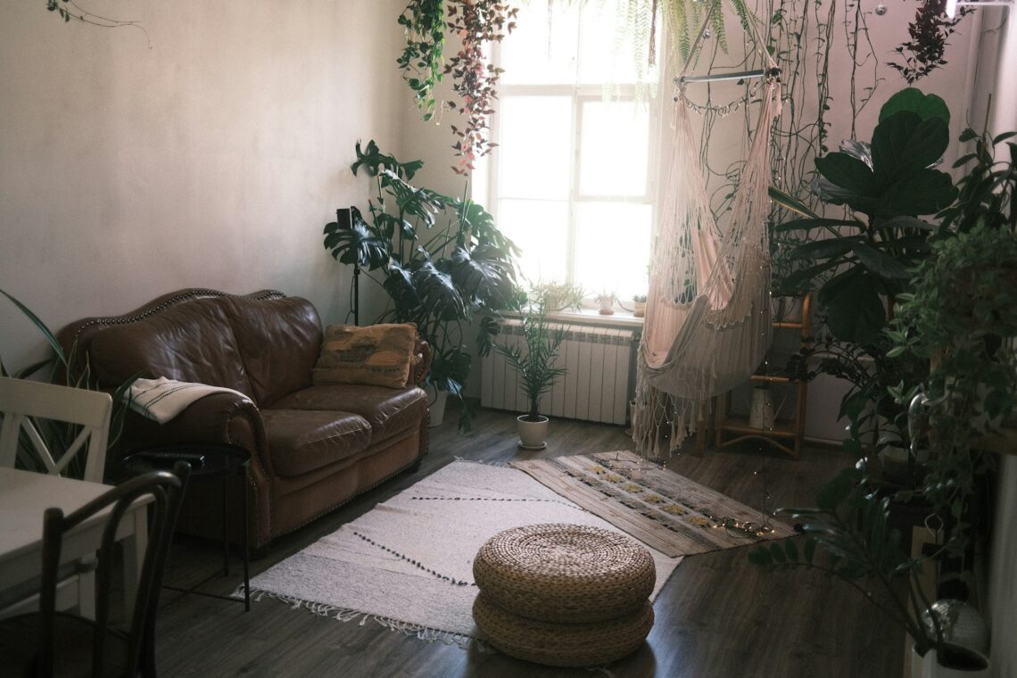 Cozy small apartment living room with vintage leather sofa, hanging plants, macrame wall decor, and wicker pouf