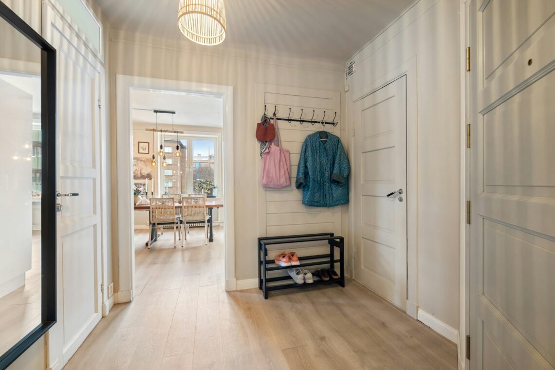 Bright Scandinavian apartment entryway with black 2-tier shoe rack, sneakers, and wall-mounted coat hooks with colorful jacket