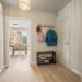 Bright Scandinavian apartment entryway with black 2-tier shoe rack, sneakers, and wall-mounted coat hooks with colorful jacket