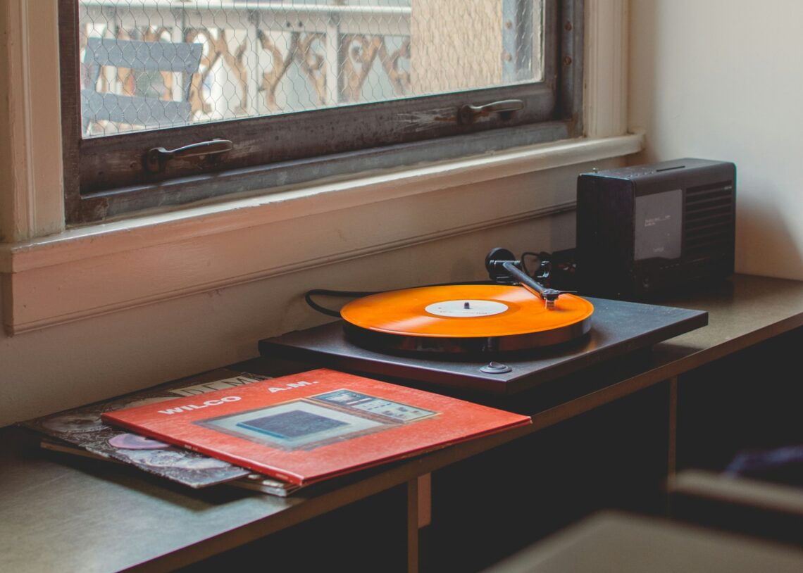 Orange vinyl record spinning on turntable by apartment window with Wilco album cover nearby